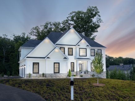 Two-story white house with black-trimmed windows and stone accents at dusk with a landscaped lawn